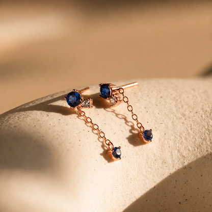 Rose gold earrings with blue gemstones on a beige surface