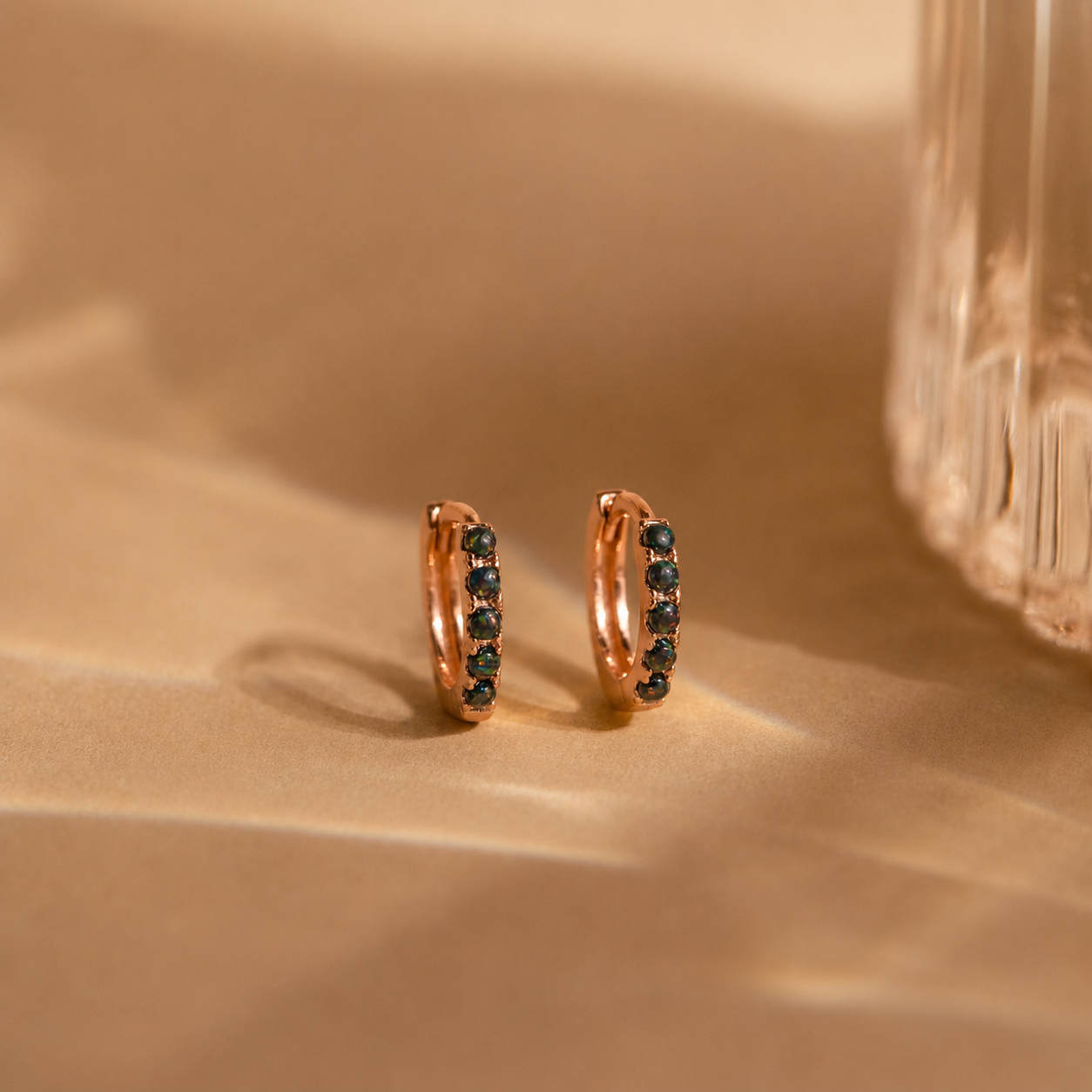 Rose gold hoop earrings with black stones on a beige surface