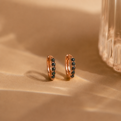 Rose gold hoop earrings with black stones on a beige surface