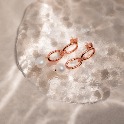 Rose gold earrings with pearls on a textured beige surface