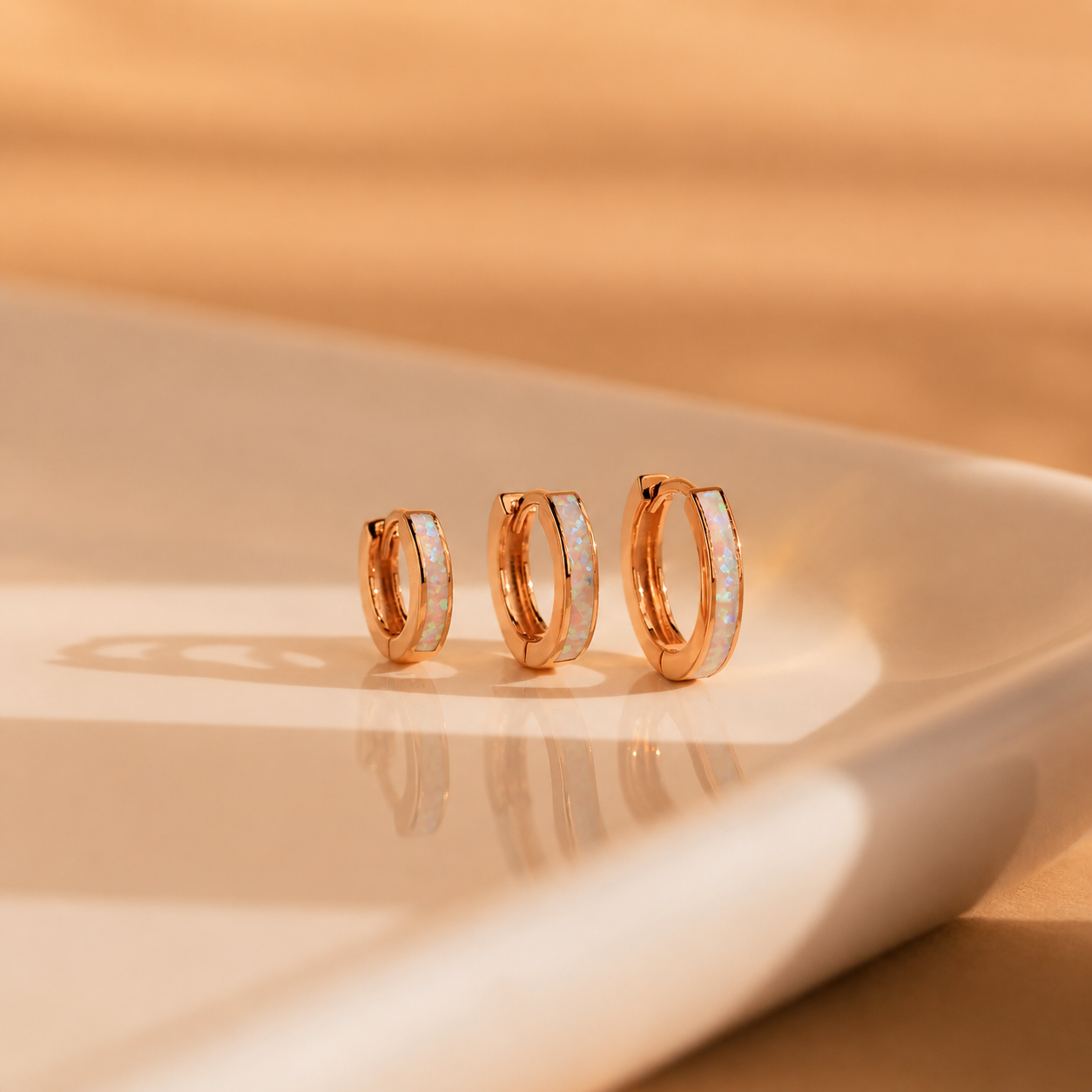 Three gold hoop earrings on a beige surface with a soft focus background