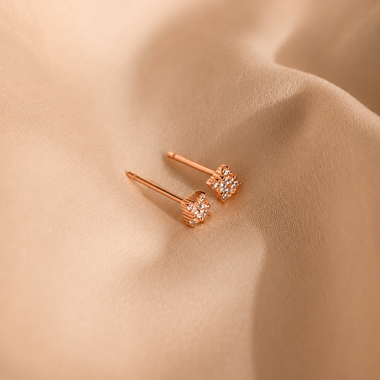 Rose gold earrings with diamond-like stones on a beige fabric background