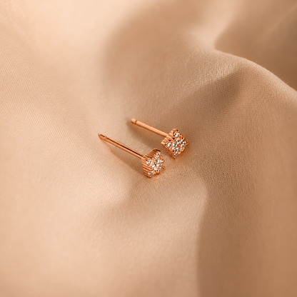 Rose gold earrings with diamond-like stones on a beige fabric background