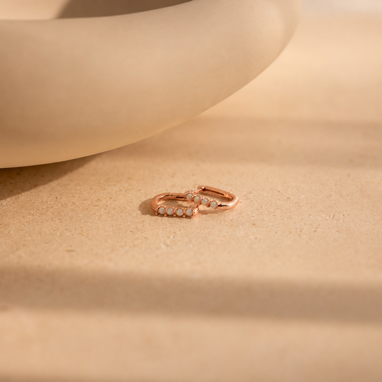 Rose gold hoop earrings with embedded stones on a beige surface