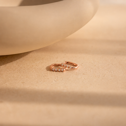 Rose gold hoop earrings with embedded stones on a beige surface
