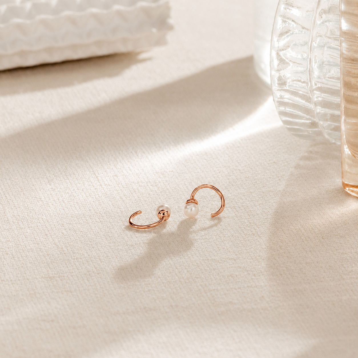Rose gold earrings with pearls on a light fabric background
