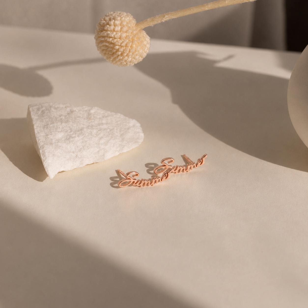 Rose gold bracelet on a textured surface with a decorative plant in the background