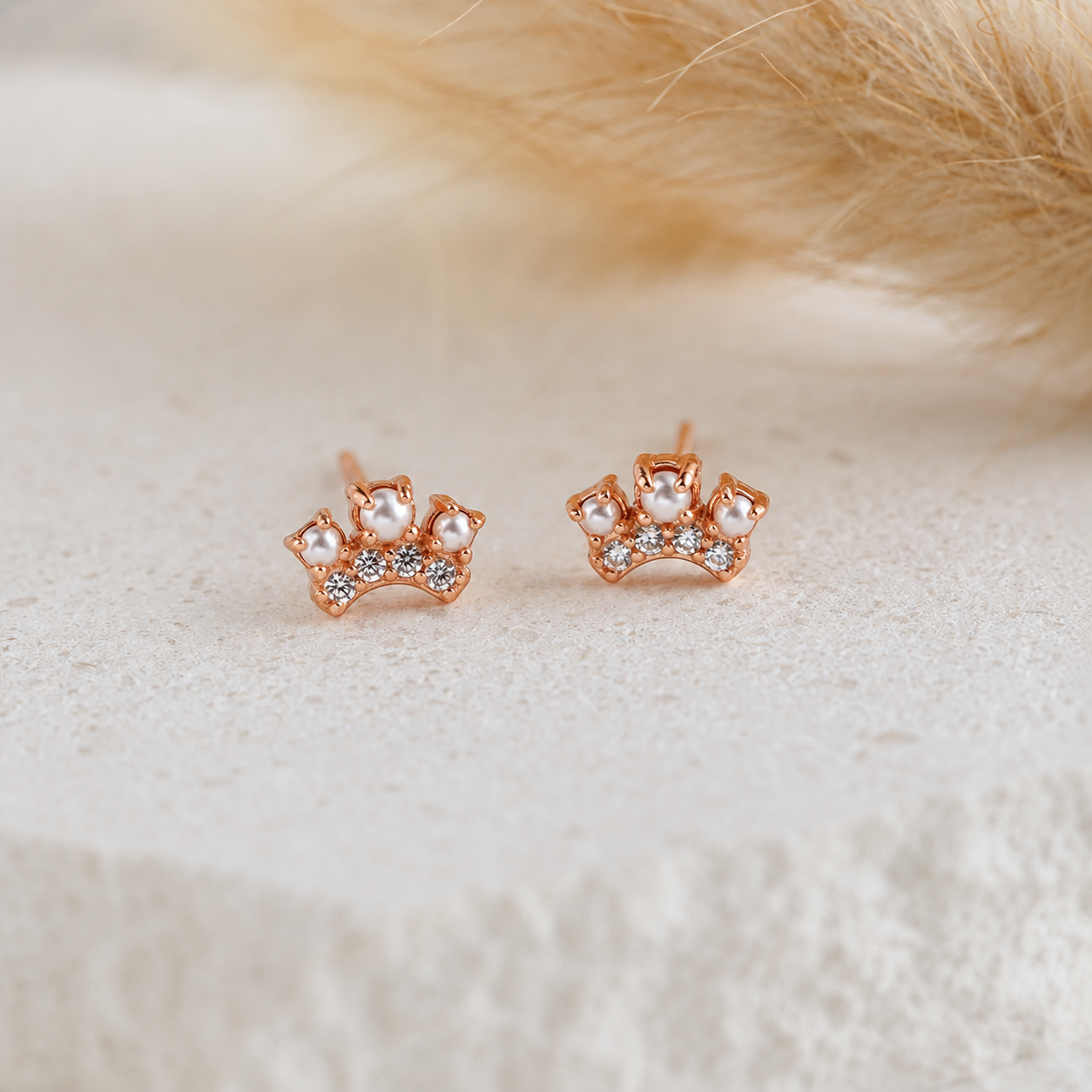 Rose gold earrings with pearl-like stones on a soft white background