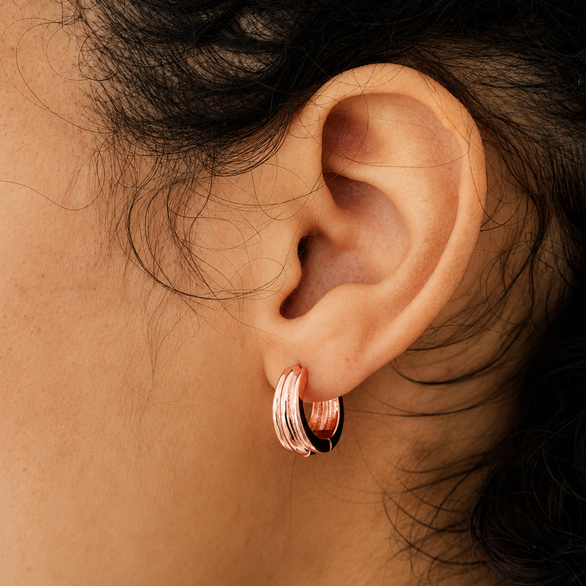 Close-up of an ear wearing a rose gold hoop earring with dark hair partially visible.