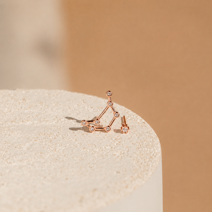 Rose gold geometric earrings on a beige stone surface with a soft brown background