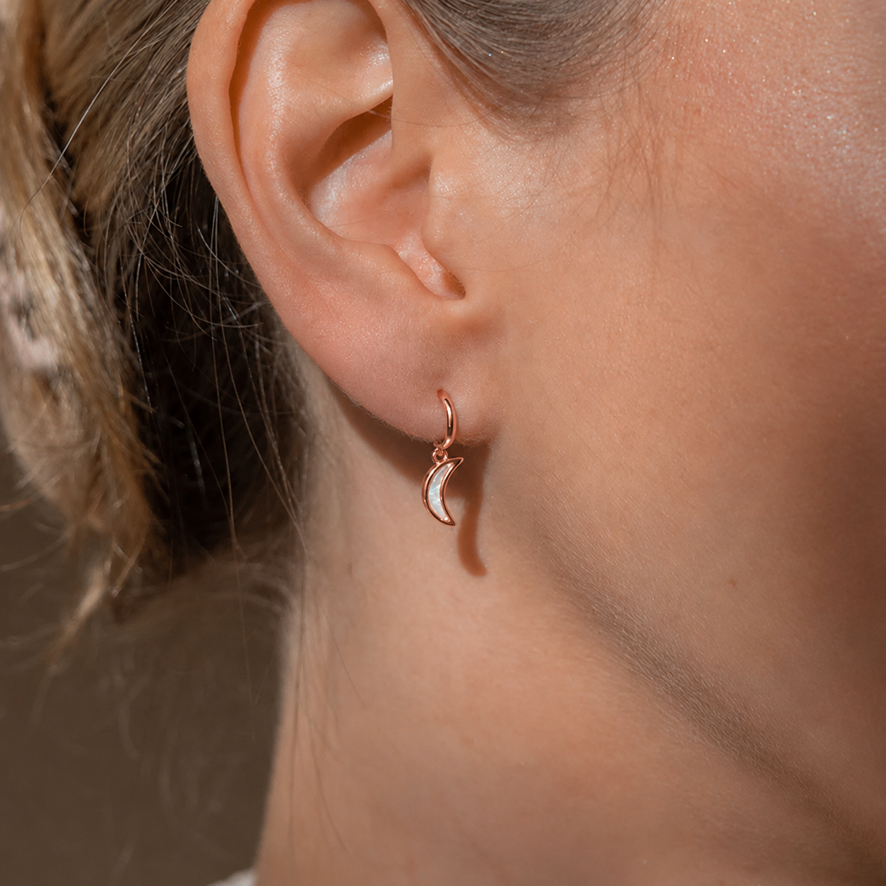 Close-up of an ear wearing a small hoop earring with a crescent moon design.