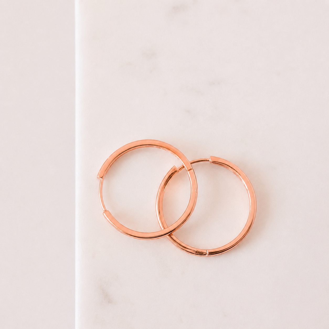 Rose gold hoop earrings on a light pink background
