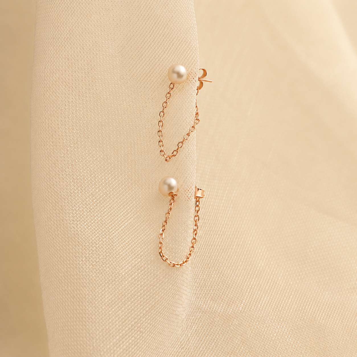 Pair of pearl earrings with gold chains on a beige fabric background
