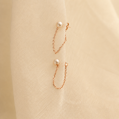 Pair of pearl earrings with gold chains on a beige fabric background