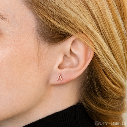 Close-up of an ear wearing a gold letter 'A' earring with blonde hair.