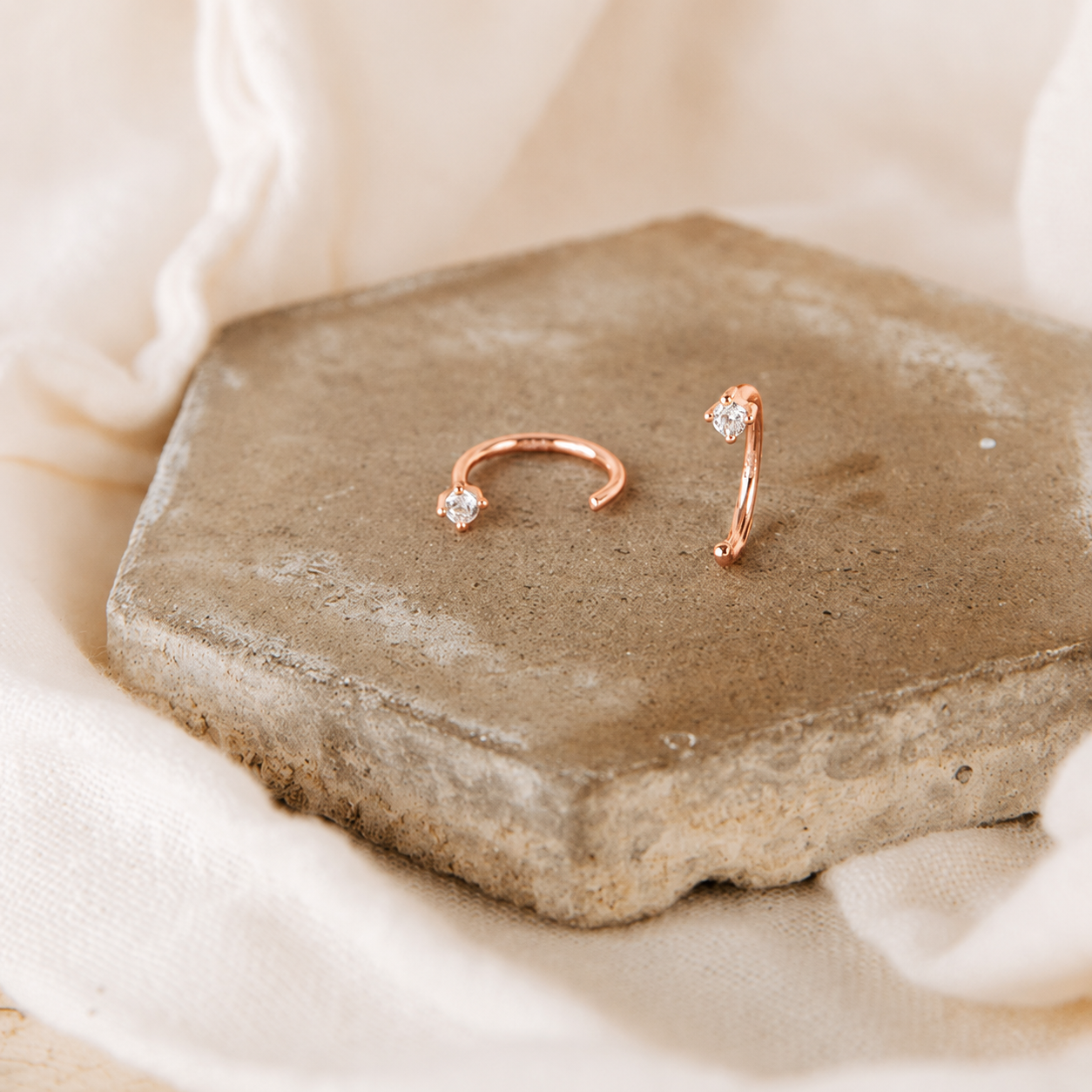 Rose gold hoop earrings on a stone surface with a soft beige background