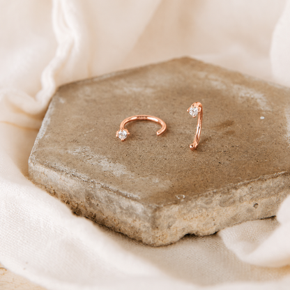 Rose gold hoop earrings on a stone surface with a soft beige background