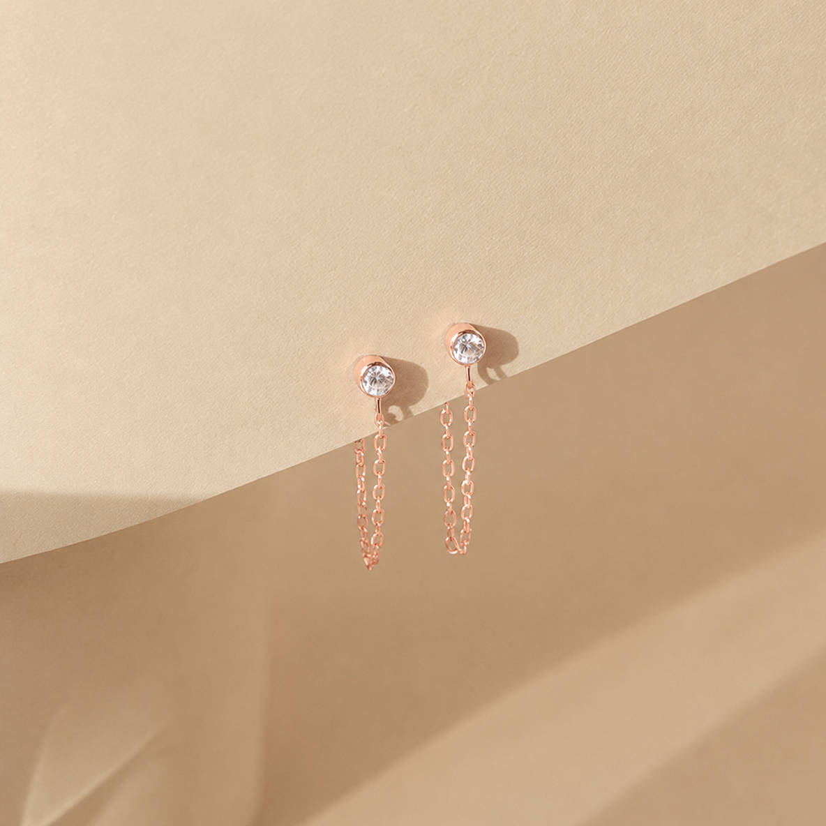 Rose gold earrings with chain details on a beige background