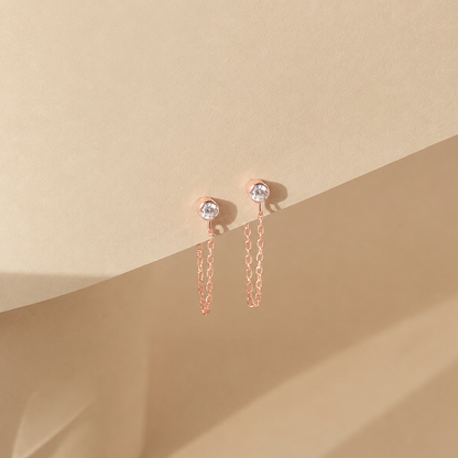 Rose gold earrings with chain details on a beige background