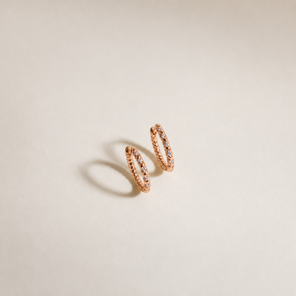 Rose gold hoop earrings with embedded stones on a beige background