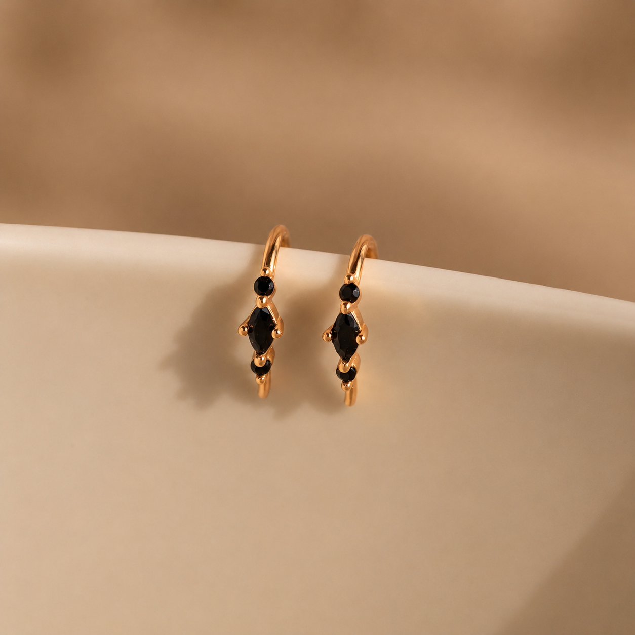 Gold hoop earrings with black gemstones on a beige surface