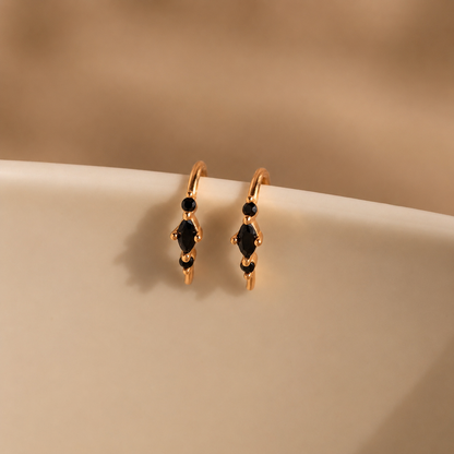 Gold hoop earrings with black gemstones on a beige surface
