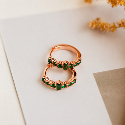 Rose gold ring with green gemstones on a light background