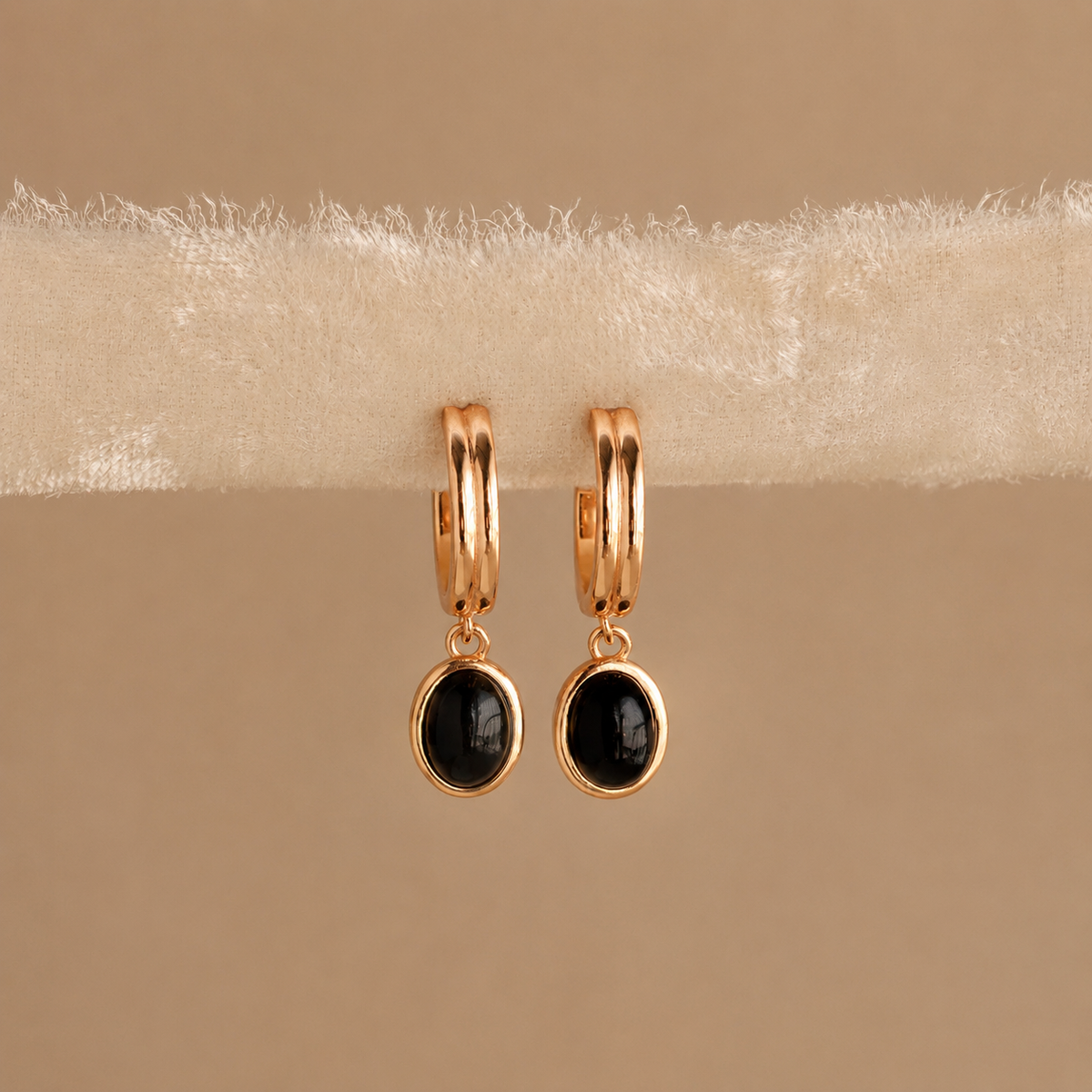 Gold hoop earrings with black gemstones on a beige surface