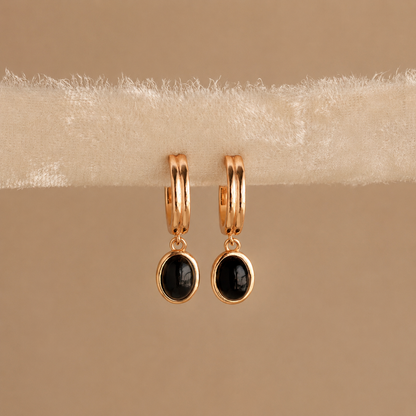 Gold hoop earrings with black gemstones on a beige surface
