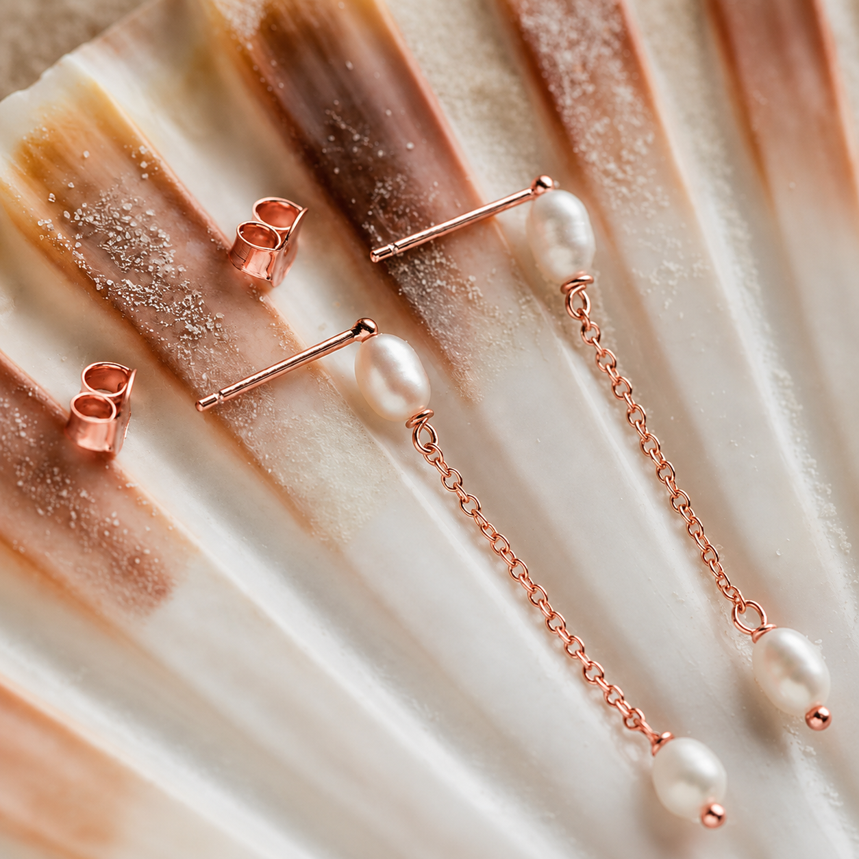 Rose gold jewelry set with bar and chain design on a textured beige surface