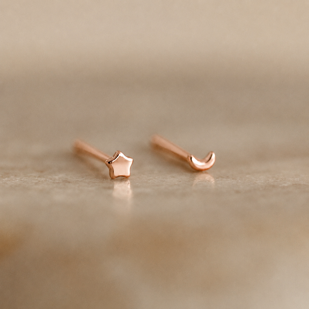 Rose gold star and moon earrings on a beige background