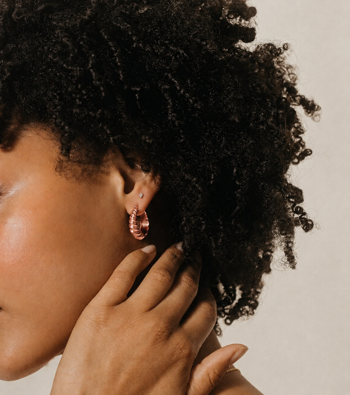 Close-up of a person with textured hair wearing pink earrings against a neutral background
