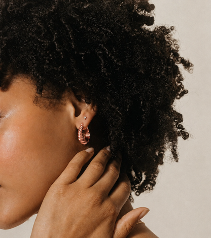 Close-up of a person with textured hair wearing pink earrings against a neutral background