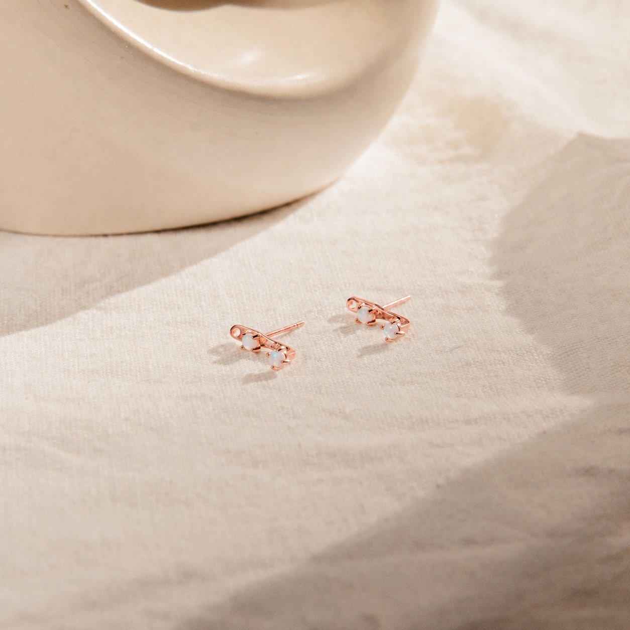 Rose gold earrings on a beige fabric background