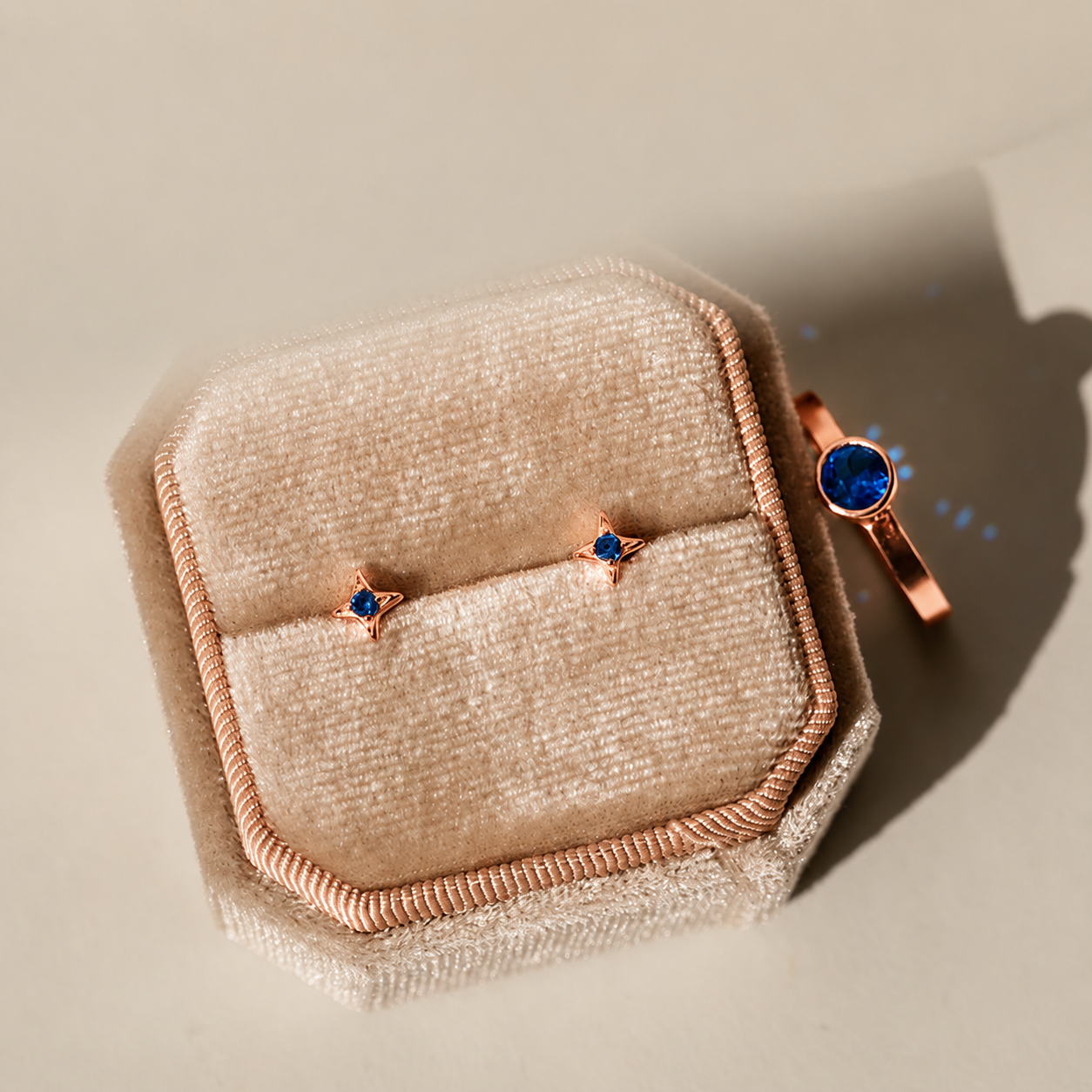 Pair of rose gold earrings with blue gemstones on a beige textured surface
