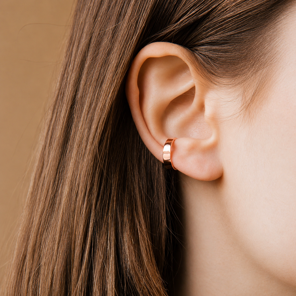 Close-up of an ear wearing a gold hoop earring with brown hair.