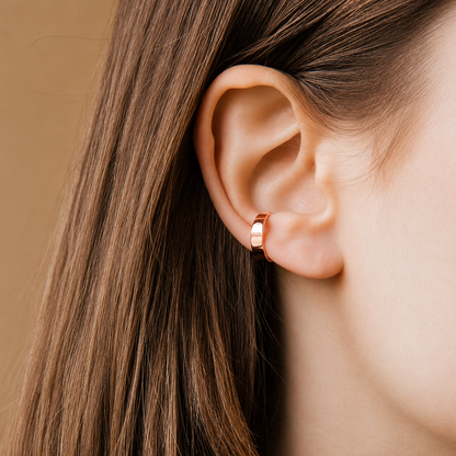 Close-up of an ear wearing a gold hoop earring with brown hair.
