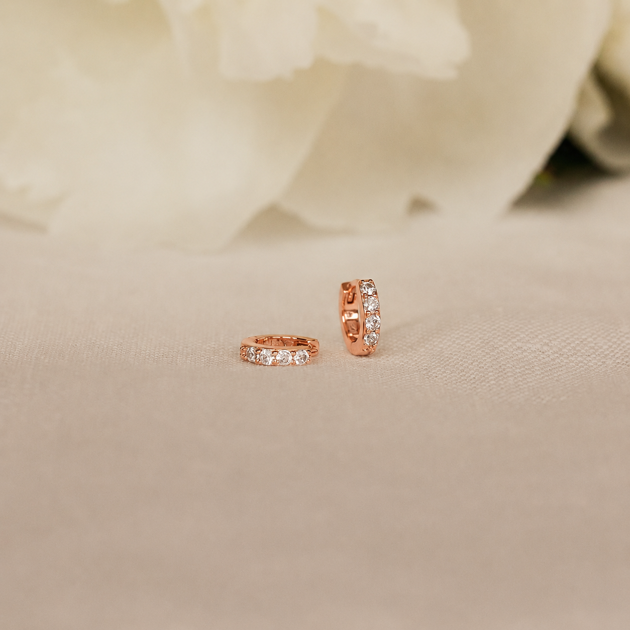 Rose gold hoop earrings with embedded diamonds on a beige fabric background