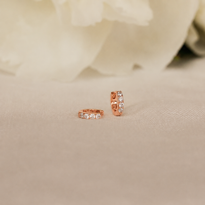 Rose gold hoop earrings with embedded diamonds on a beige fabric background