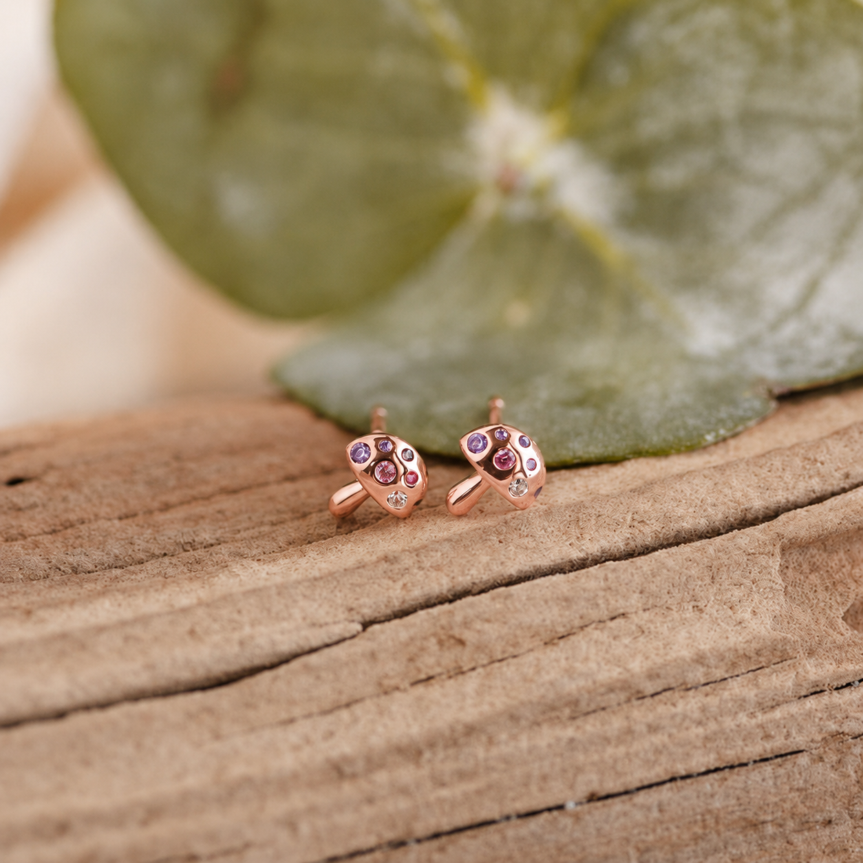 Rose gold earrings with gemstones on a wooden surface with a leaf in the background