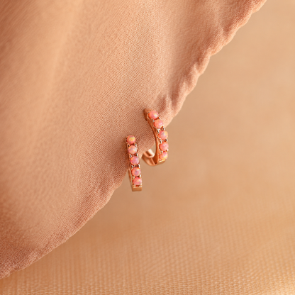 Rose gold earrings with pink gemstones on a beige fabric background