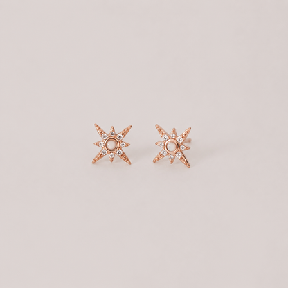 Rose gold star-shaped earrings with small diamonds on a light beige background