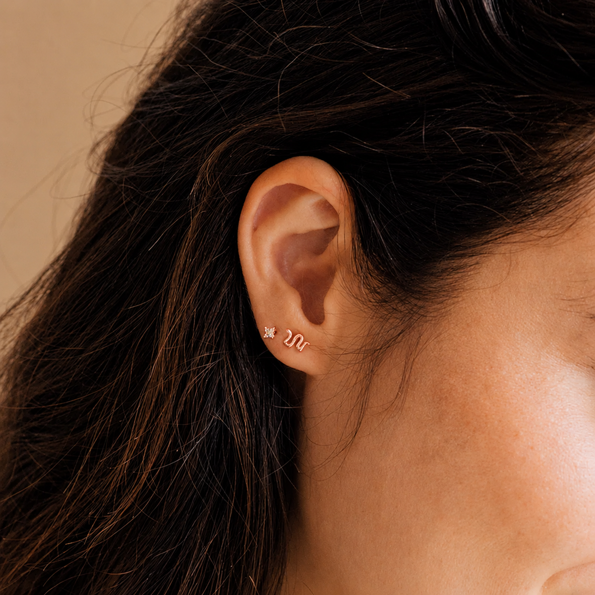 Close-up of an ear wearing a gold earring with a star design on a beige background