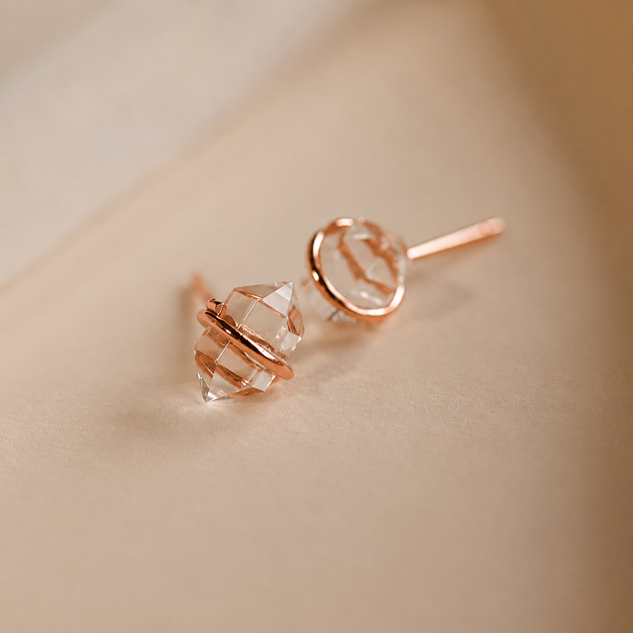 Rose gold earrings with clear gemstones on a beige background