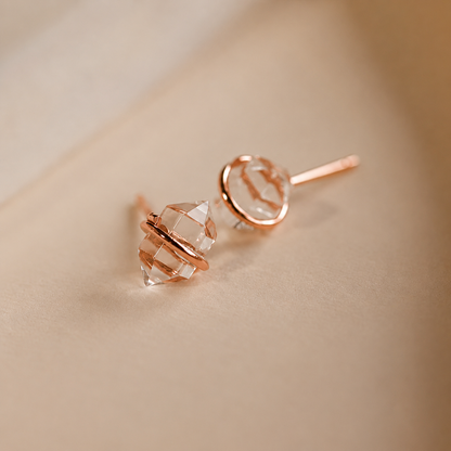 Rose gold earrings with clear gemstones on a beige background