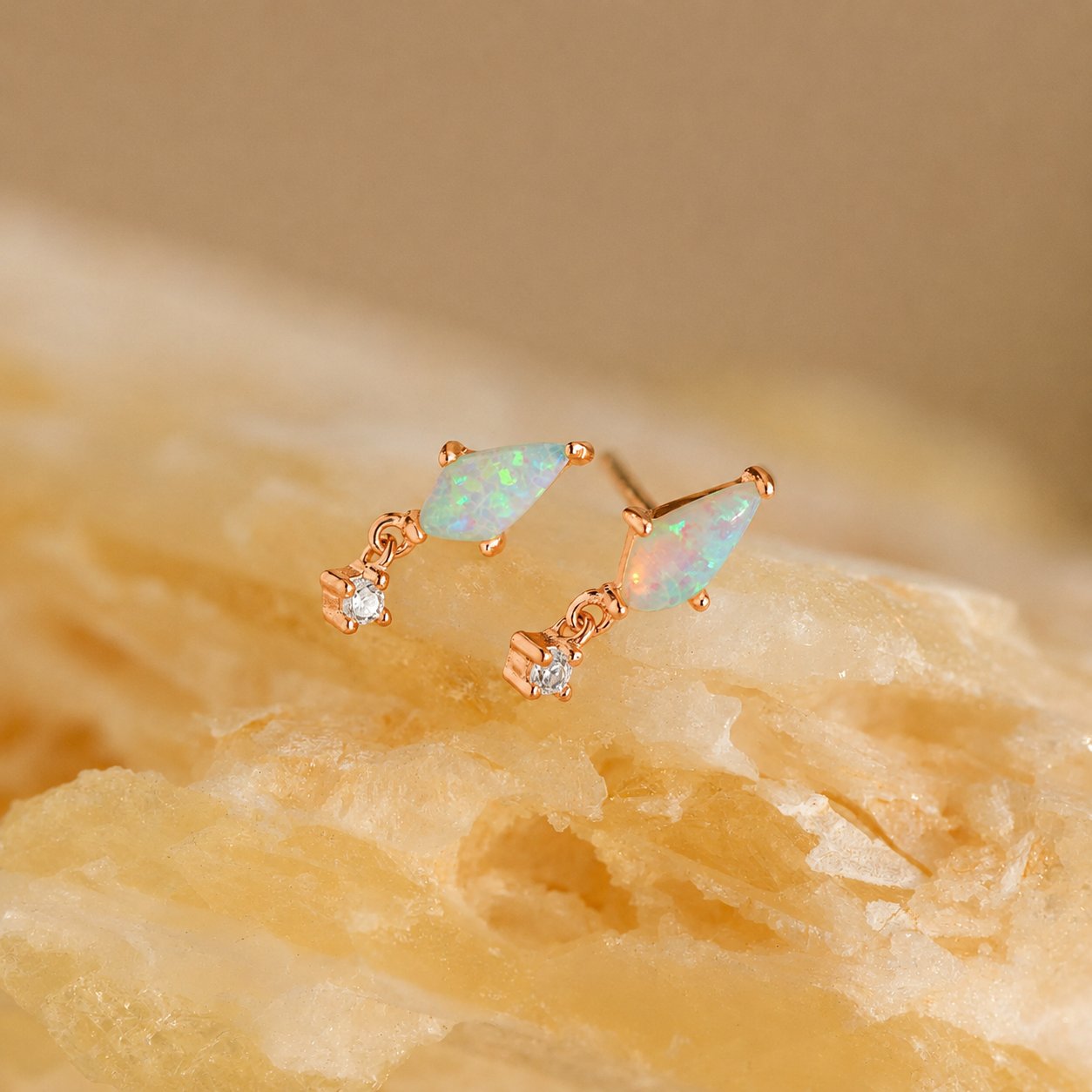 Pair of gold earrings with opal stones on a beige stone background