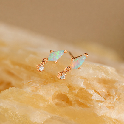 Pair of gold earrings with opal stones on a beige stone background
