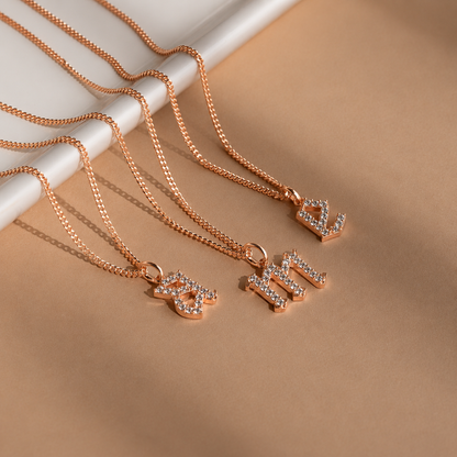 Rose gold necklaces with letter pendants on a beige surface