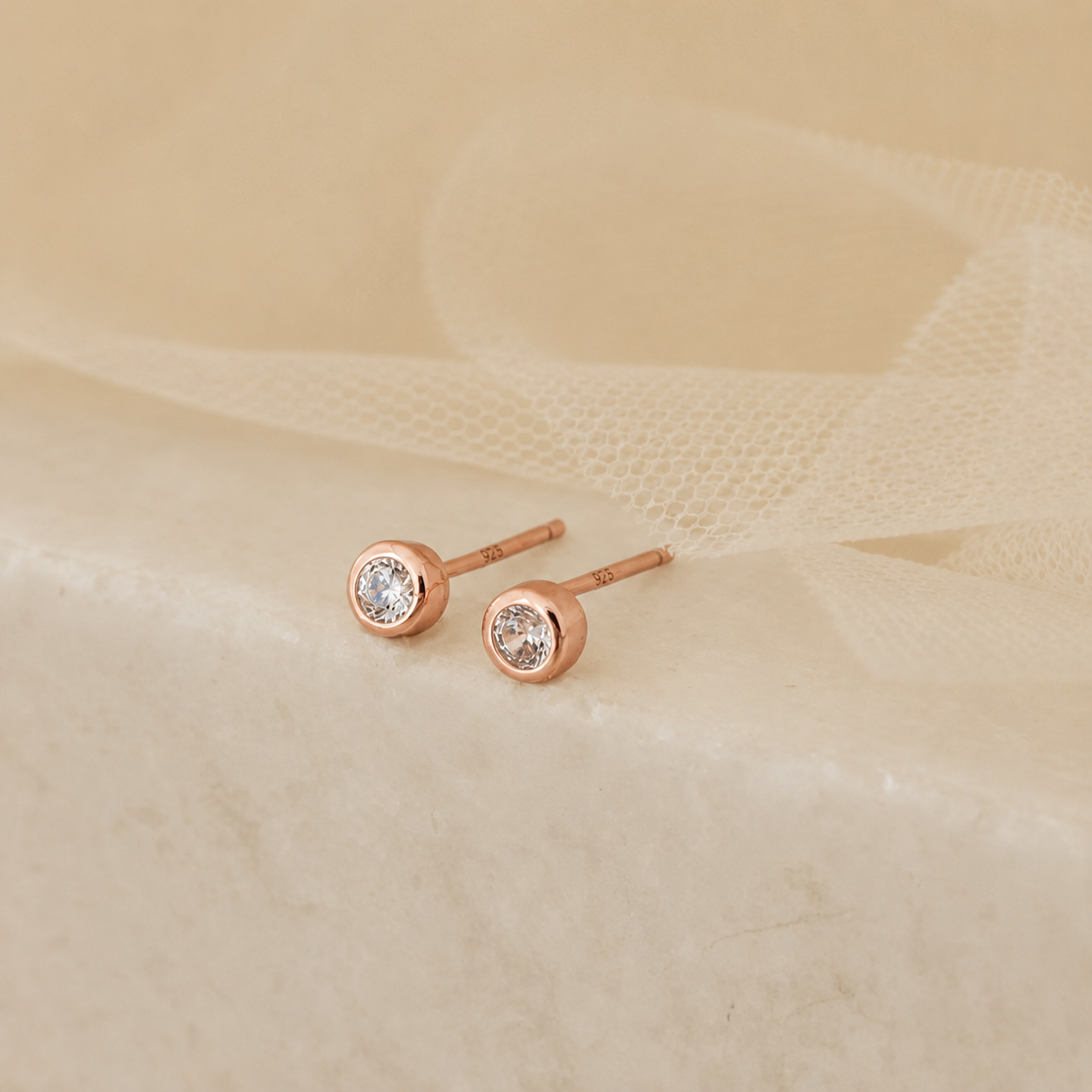 Rose gold earrings with clear gemstones on a beige fabric background