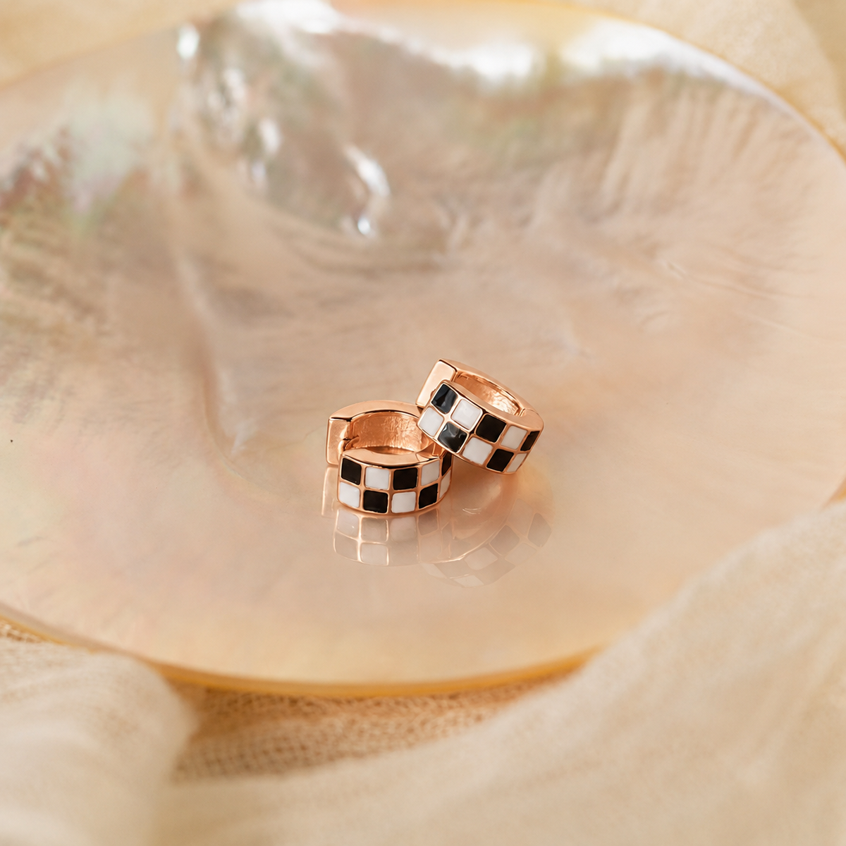 Pair of rose gold hoop earrings with black and white checkered pattern on a shell background
